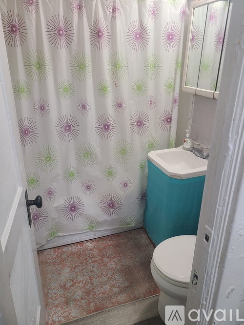 A bathroom with a toilet, a shower curtain with a flower pattern, and a tiled floor.