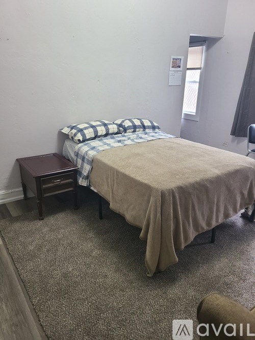 A bed with a blanket and pillow is in the corner of a room with a carpeted floor.