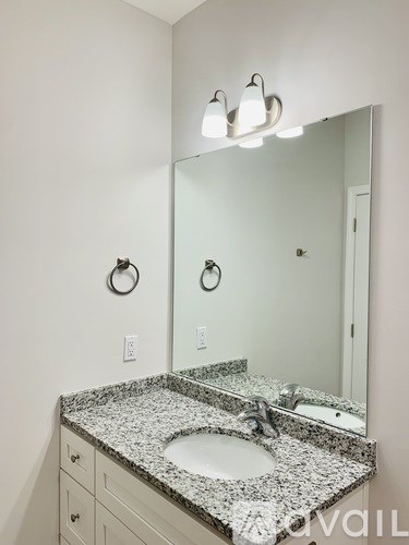 A bathroom with a granite counter top and a round mirror.