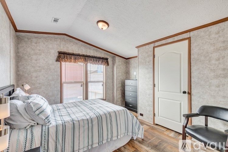 A bedroom with a bed, chair, and a window with curtains.