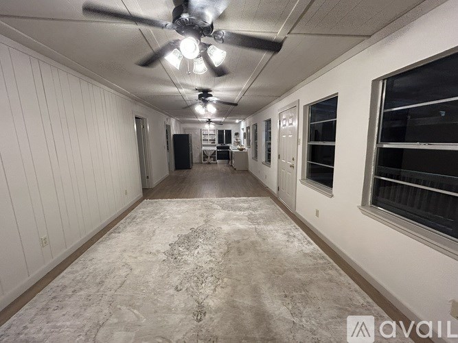 A long, empty hallway with a rug on the floor and a ceiling fan above.