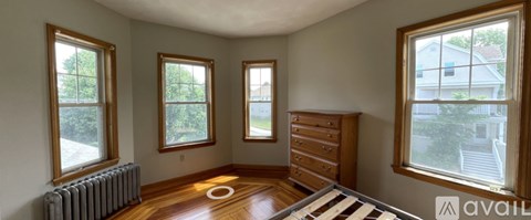 A room with a radiator, a dresser, and three windows.
