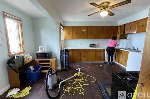 A woman in a pink shirt is vacuuming a kitchen.