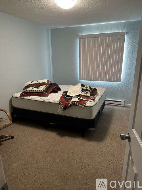 A bedroom with a bed, carpet, and a window with blinds.