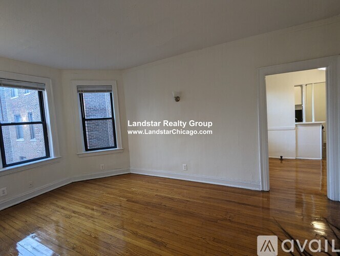 A room with wooden floors and white walls, with a window on the left and a door on the right.