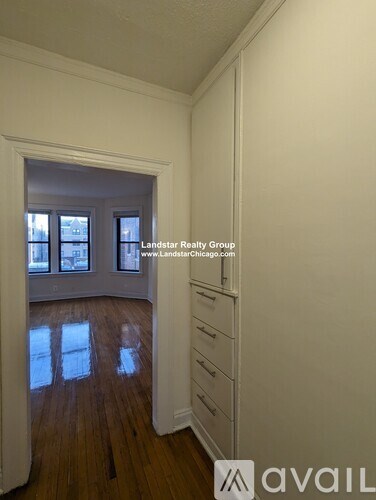 A room with wooden floors and white walls, with a window and a doorway leading to another room.