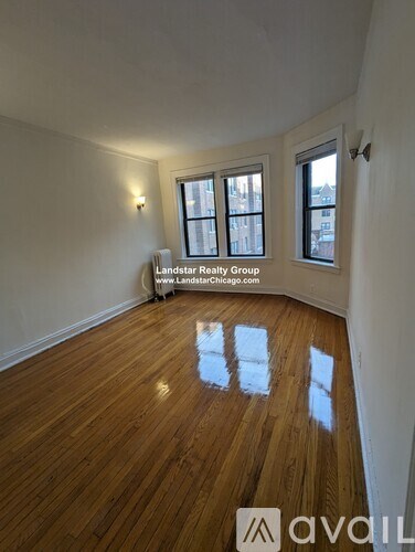 A room with wooden flooring and two windows, with a sign for Landstar Realty Group.