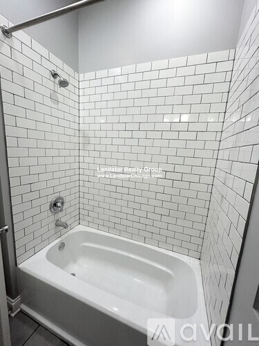 A white tiled bathroom with a white bathtub and a shower head.