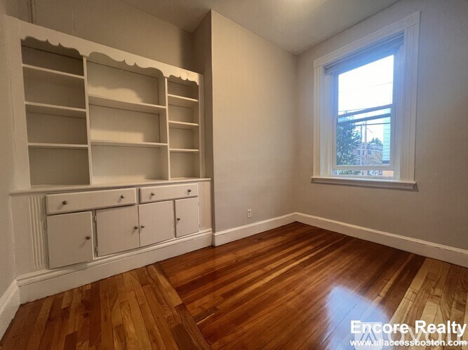 A room with wooden floors and a window with a view of a building outside.