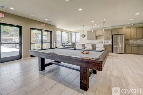 A pool table is in the middle of a room with a kitchen in the background.