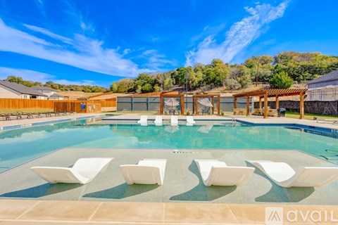 A pool with white chairs and a wooden pergola.