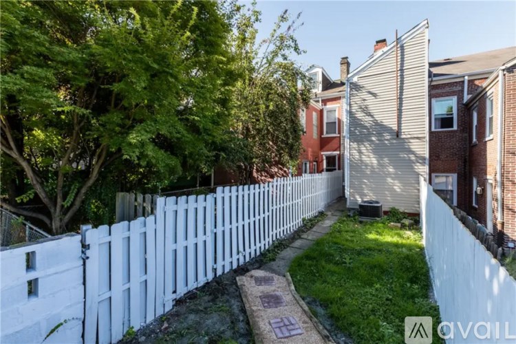 A white picket fence separates a green lawn from a red brick house.
