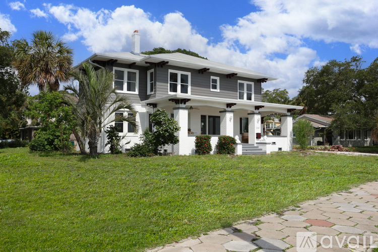 A house with a grey roof and white trim is surrounded by a green lawn.