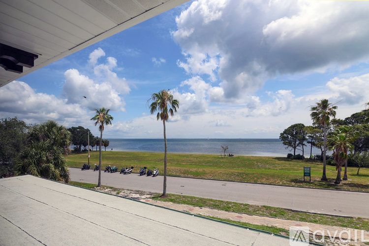 A view of a beach from a balcony with palm trees and a parking lot.