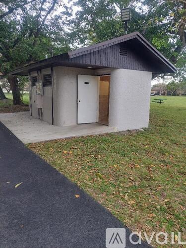 A small building with a brown roof and a white door is situated in a grassy area.