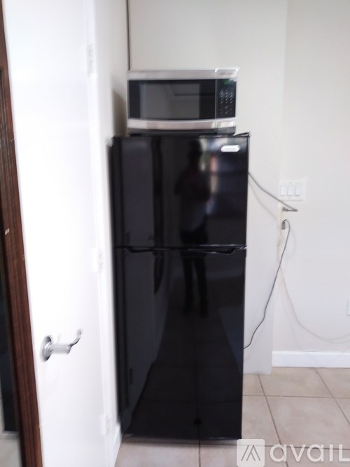 A black fridge with a microwave on top.