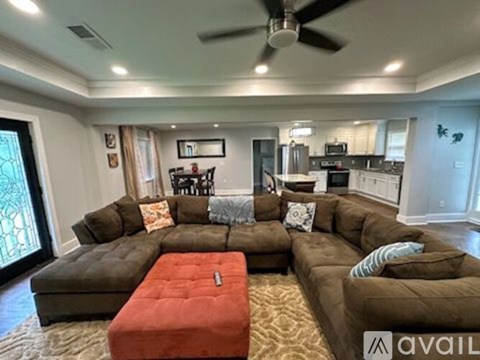 A living room with a brown sectional sofa and a red ottoman.