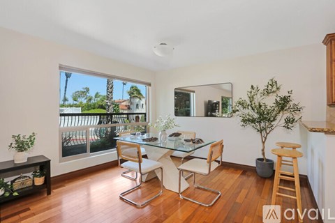 A dining room with a glass table and chairs, a potted plant, and a view of the outdoors through a sliding glass door.