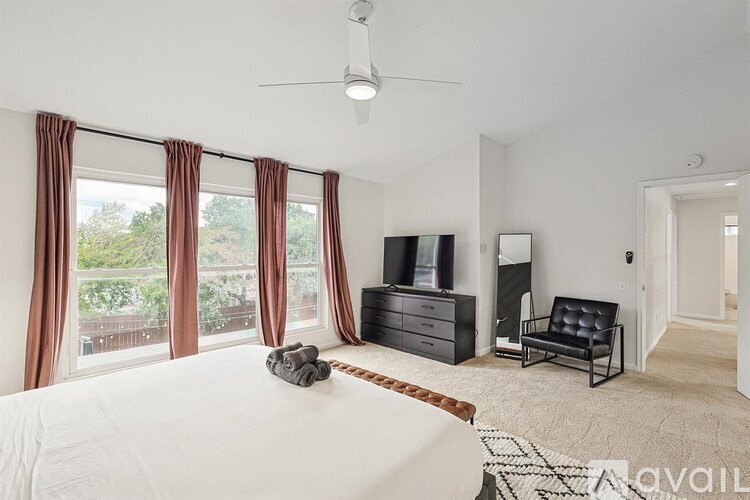 A bedroom with a large bed, a television, a chair, and a window with curtains.
