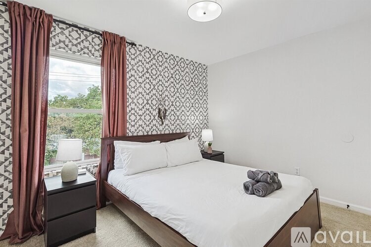 A bedroom with a large bed, a nightstand with a lamp, and a window with curtains.