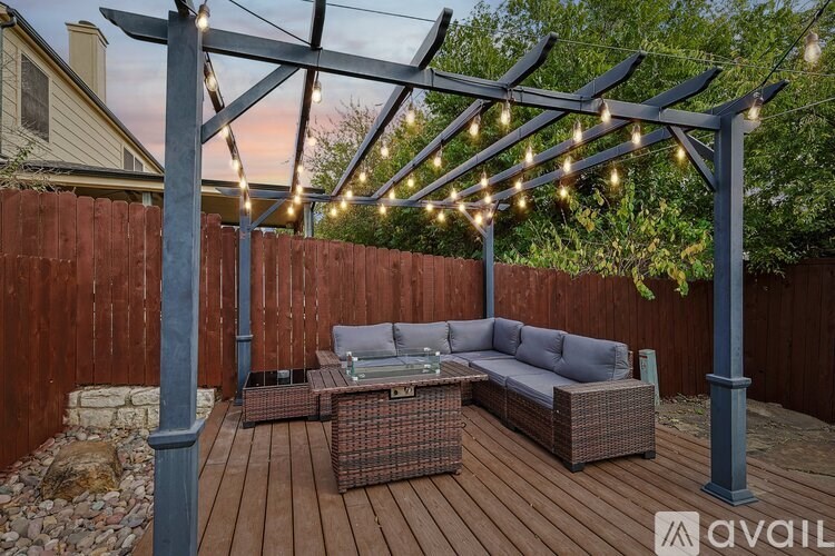 A patio with a couch and a table under a pergola with lights.