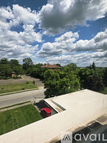 A view from a high vantage point looking down at a red car and a building surrounded by trees.