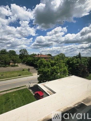 A view from a high vantage point looking down at a red car and a building surrounded by trees.