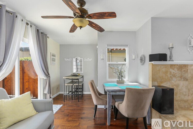 A living room with a grey couch, a dining table with chairs, a ceiling fan, and a fireplace.