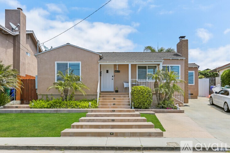 A house with a brown roof and a white door is surrounded by a green lawn and a white car is parked in the driveway.