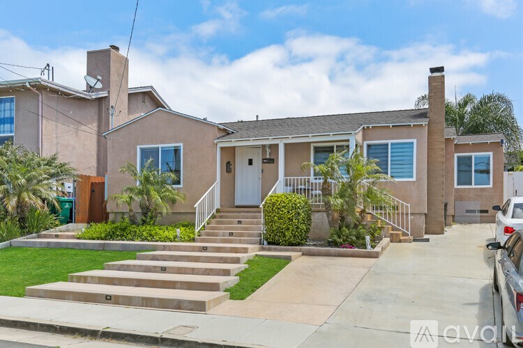 A house with a brown roof and a white door is surrounded by a green lawn and a concrete driveway.