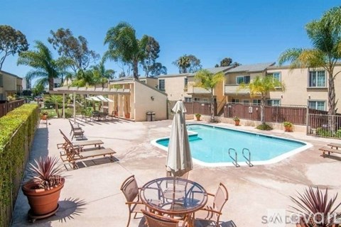 A pool surrounded by chairs and a table with an umbrella.