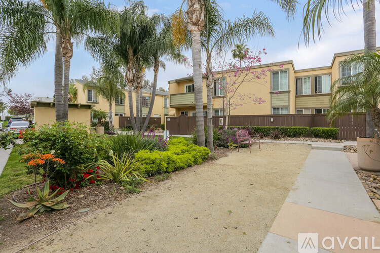 A garden with a pathway, palm trees, and a building in the background.