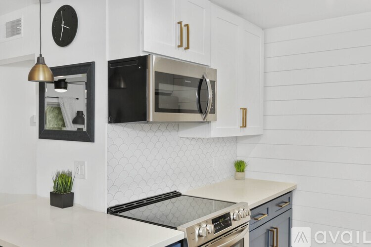 A kitchen with a black microwave above a stove and a clock on the wall.