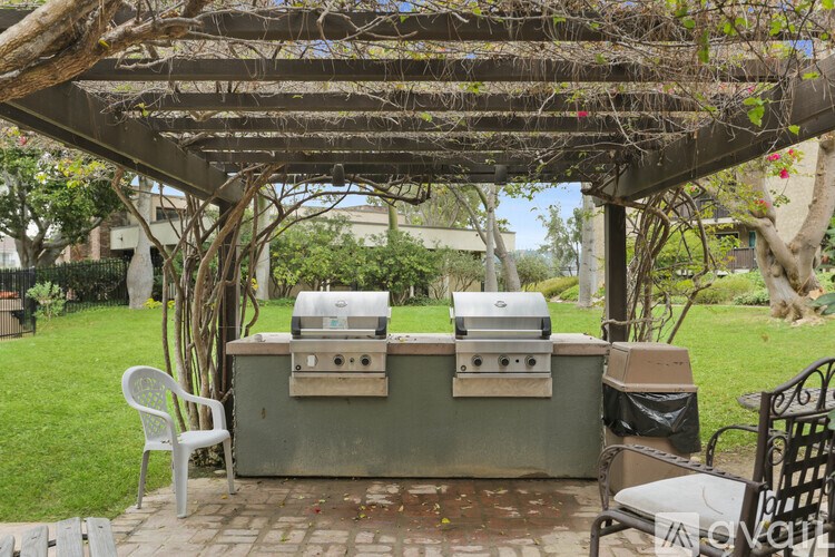 A grill is under a pergola in a backyard.