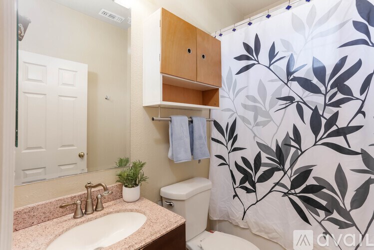 A bathroom with a sink, toilet, and a shower curtain with a leaf pattern.