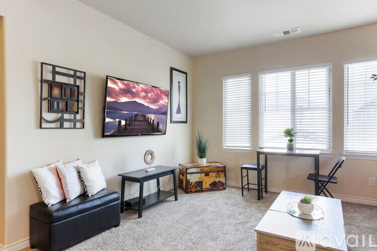 A living room with a black couch, a small table, a chair, and a painting on the wall.