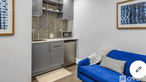 A blue couch sits in a kitchen with a microwave and oven above it.