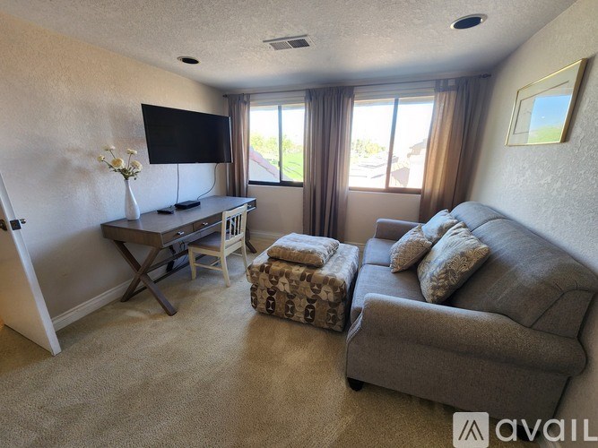 A living room with a grey couch, a wooden table, and a flat screen TV mounted on the wall.