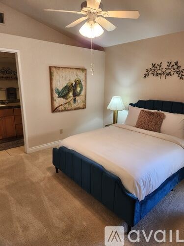 A bedroom with a bed, a ceiling fan, and a painting on the wall.