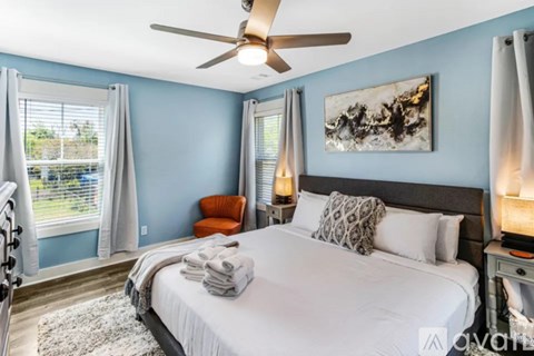 A bedroom with a large bed, a ceiling fan, and a painting on the wall.