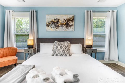 A bedroom with a large bed, a painting on the wall, and a window with curtains.