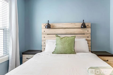 A bed with a white comforter and a green pillow is in front of a wooden headboard.