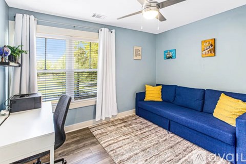 A blue couch with yellow pillows sits in a room with a ceiling fan.