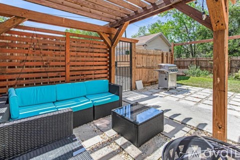 A wooden pergola with a blue couch and a black table under it.