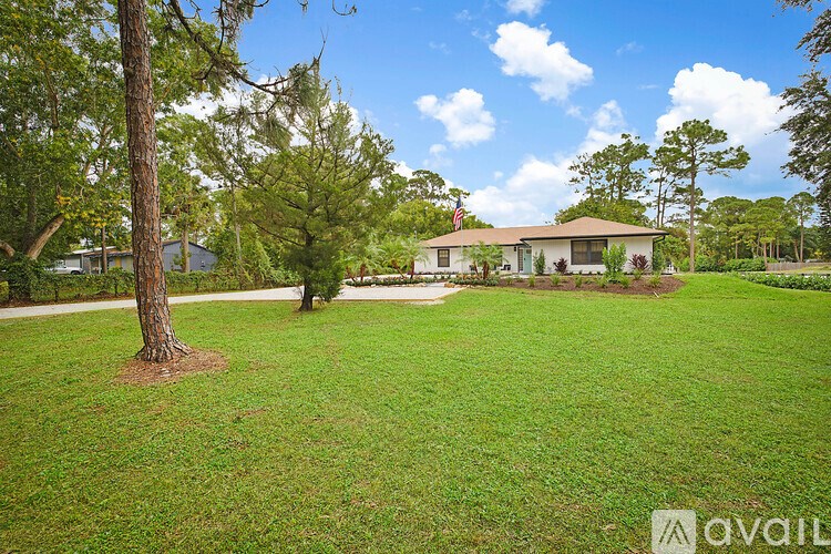 A house with a flag on the roof is surrounded by a grassy yard and trees.