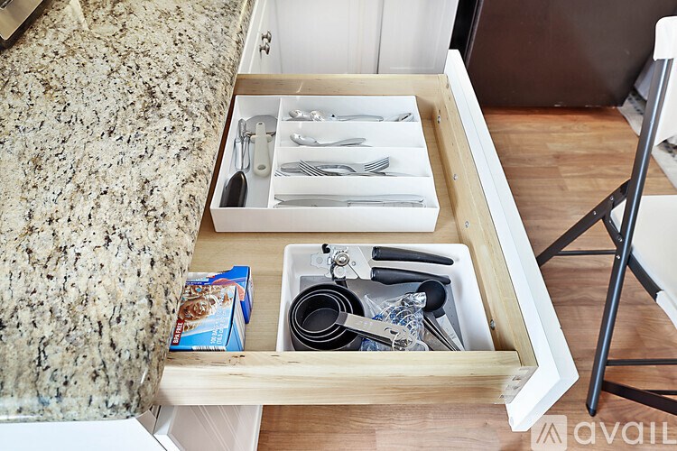 A drawer with utensils and a box of tissues is open.