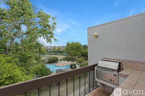 A balcony with a grill and a pool in the background.