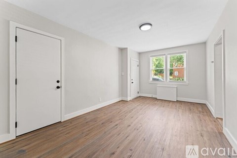 A room with wooden floors and white walls, with a window showing a view of a building outside.