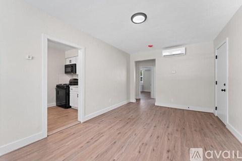 A room with wooden flooring and white walls, with a doorway leading to another room.