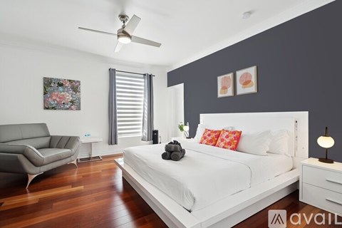 A bedroom with a white bed and a grey sofa.